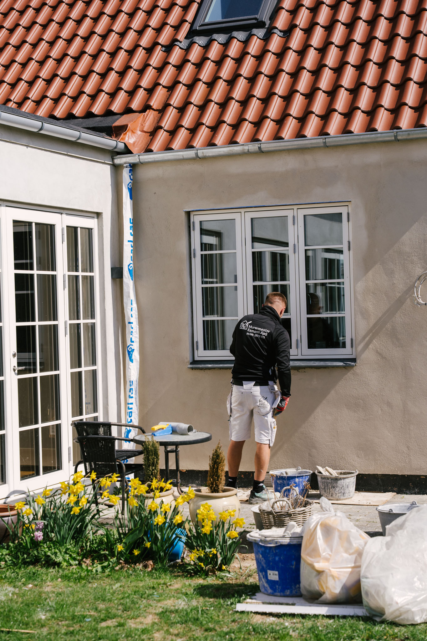 Murermester Esmann arbejder på facade på Sjælland — påskeliljer i forgrunden